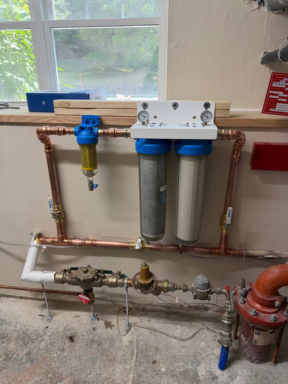 Whole-house water filtration housings with copper piping and pressure gauges on a wall