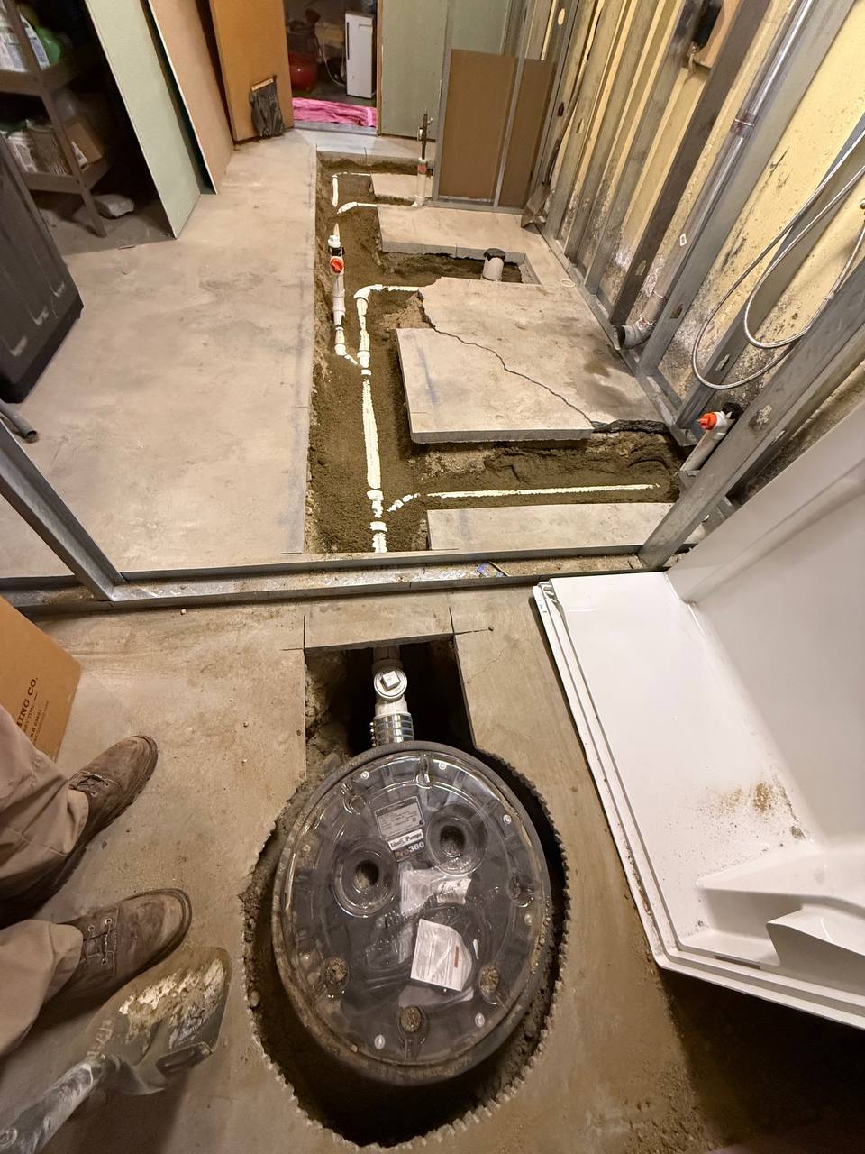 Sewage ejector pit and PVC drain lines trenched into a basement concrete floor