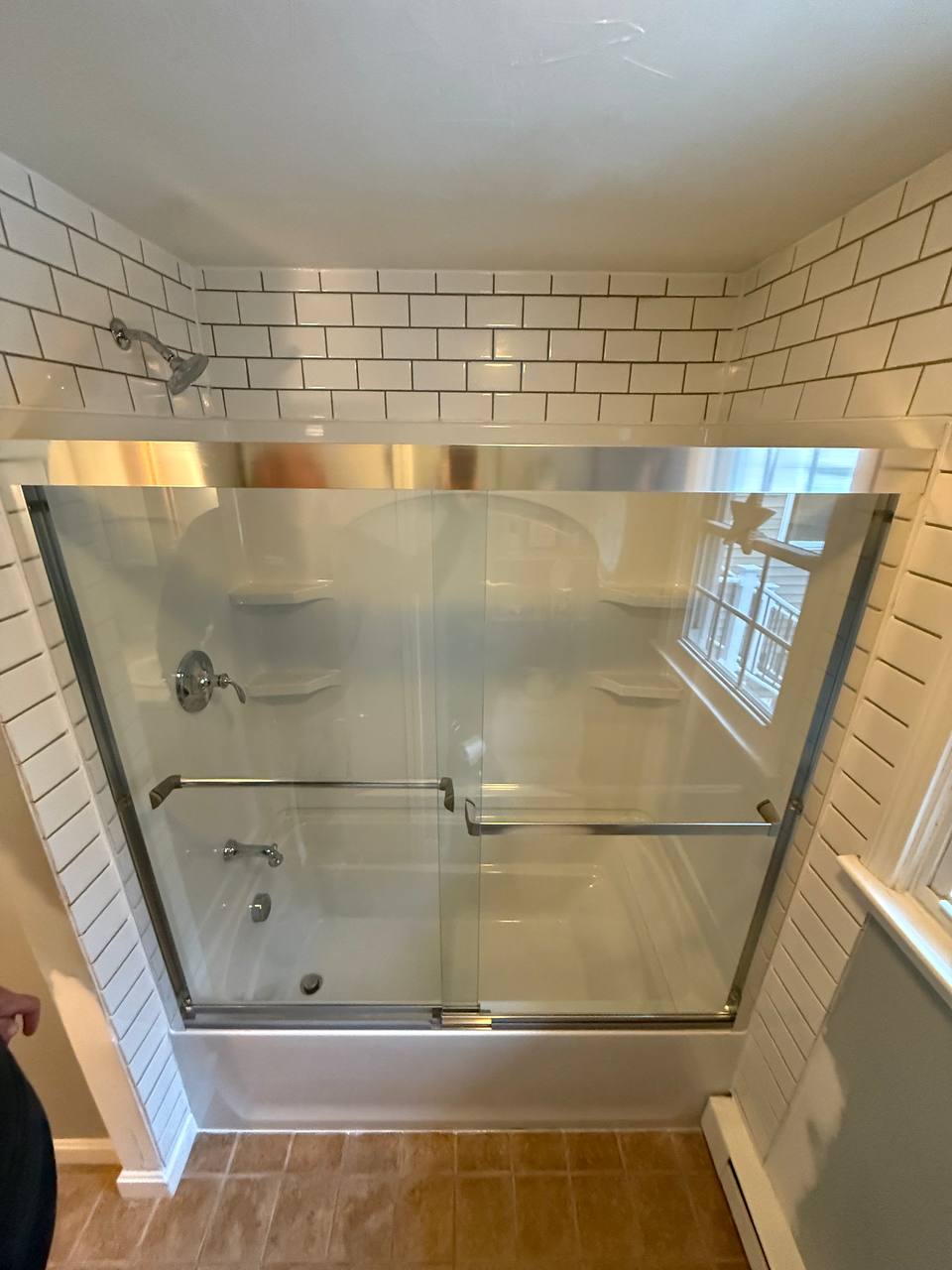 Bathtub with sliding glass shower doors and white subway tile surround