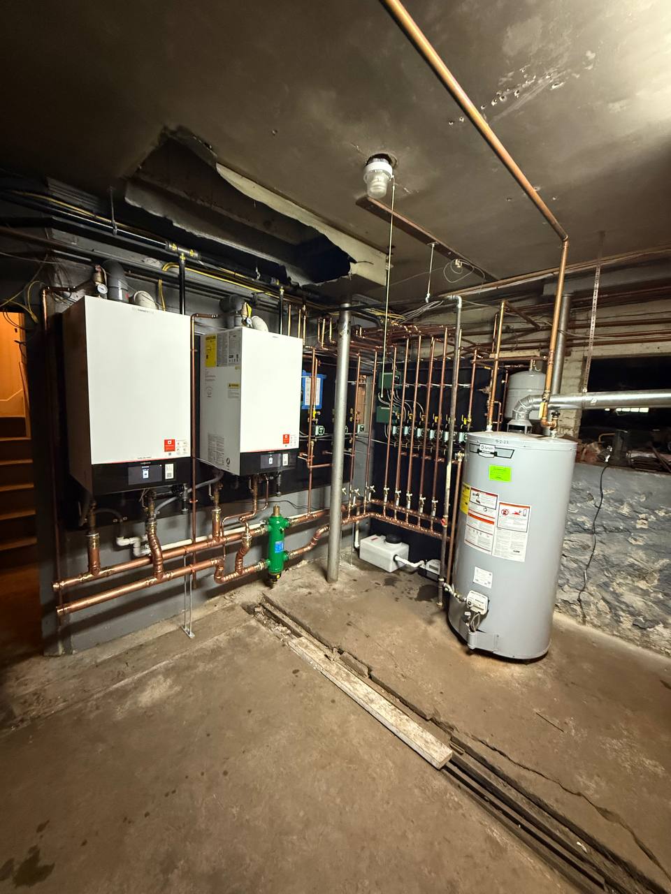 Two wall-mounted boilers with copper piping and a water heater in a basement