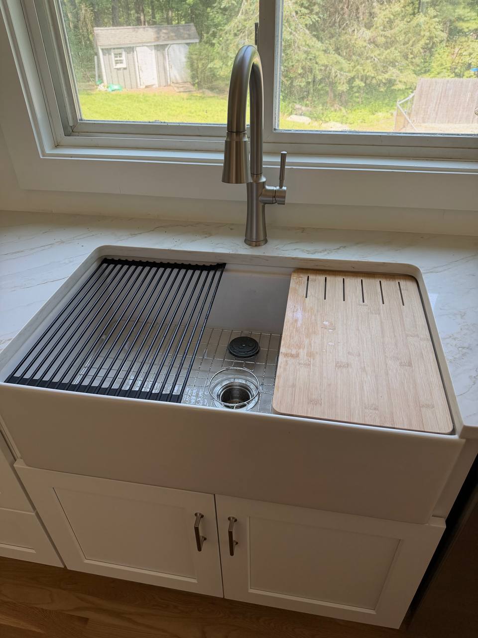White farmhouse apron-front kitchen sink with stainless pull-down faucet by a window
