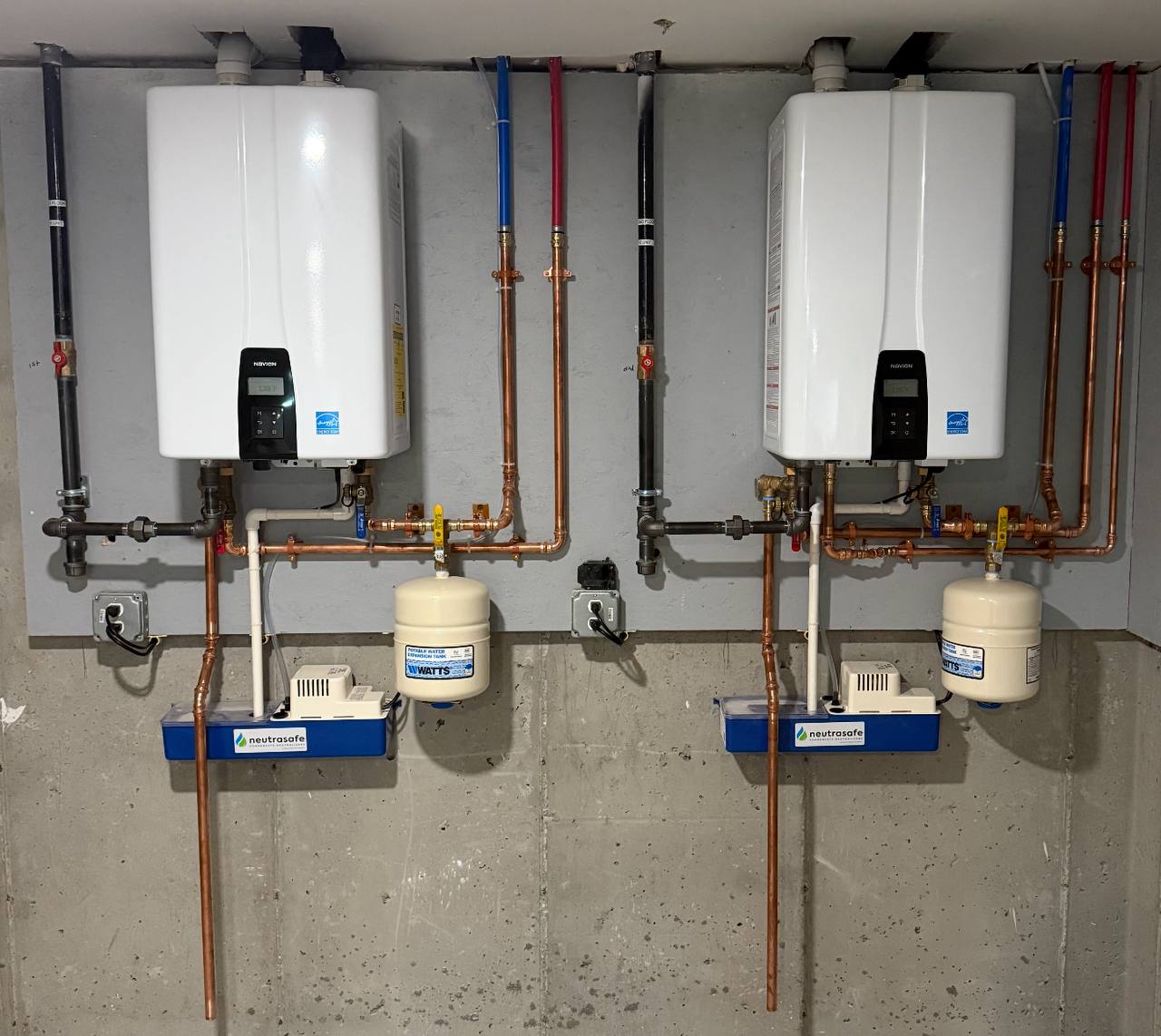 Two tankless water heaters with copper piping and expansion tanks in a basement
