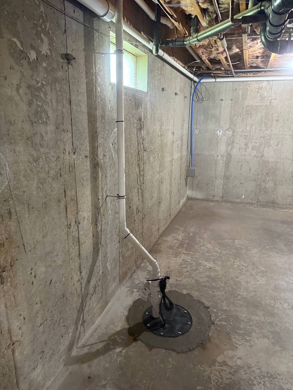 Sump pump with sealed basin lid and PVC discharge pipe in a concrete basement