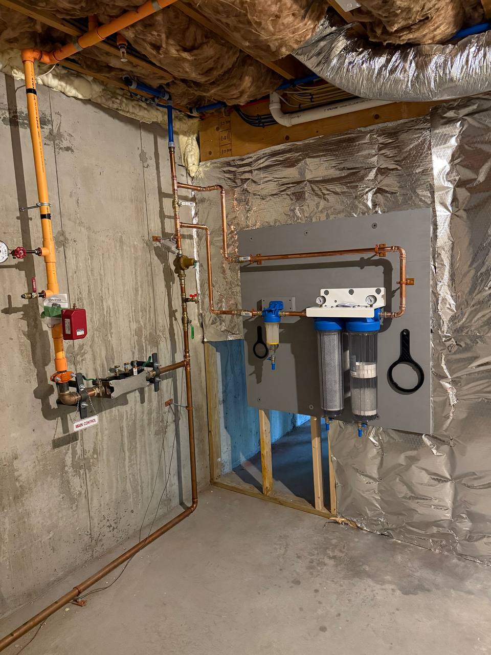 Whole-house water filtration housings and copper piping on a basement wall