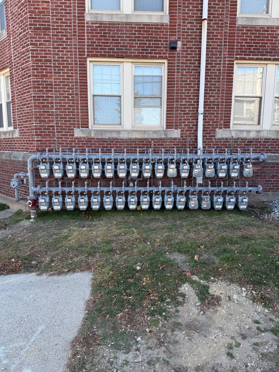 Bank of gas meters and piping mounted on an exterior brick building wall