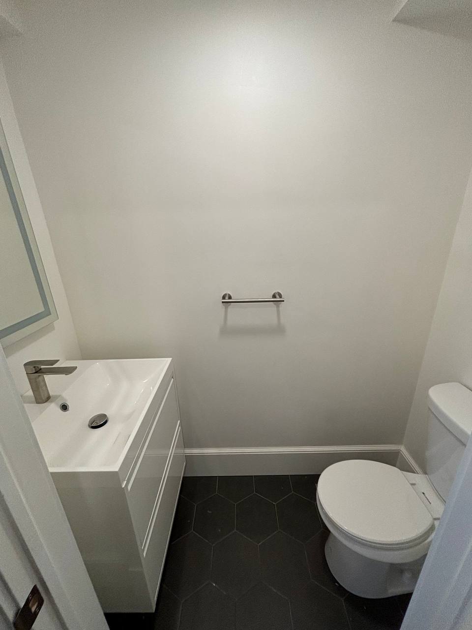 Powder room with white wall-mounted vanity and toilet on dark hexagon tile floor
