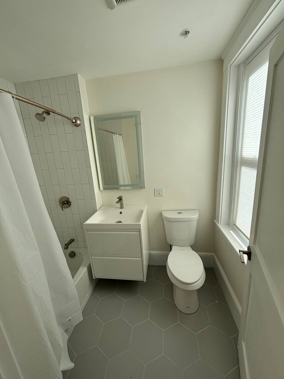Bathroom with tub-shower, curved curtain rod, wall-mounted vanity and window