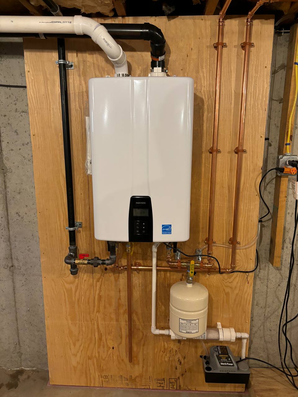 Wall-mounted tankless water heater on plywood with copper piping and expansion tank