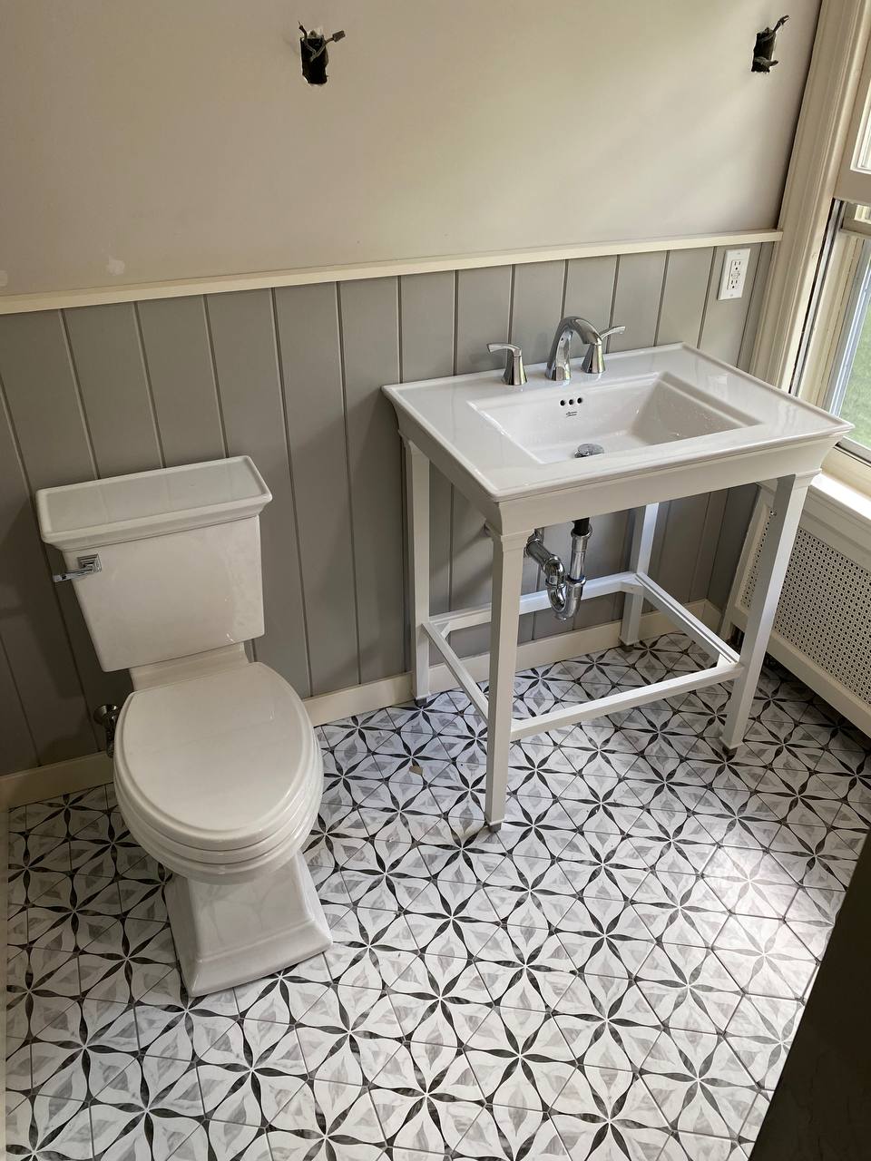 Console sink and toilet on patterned tile with gray wainscoting