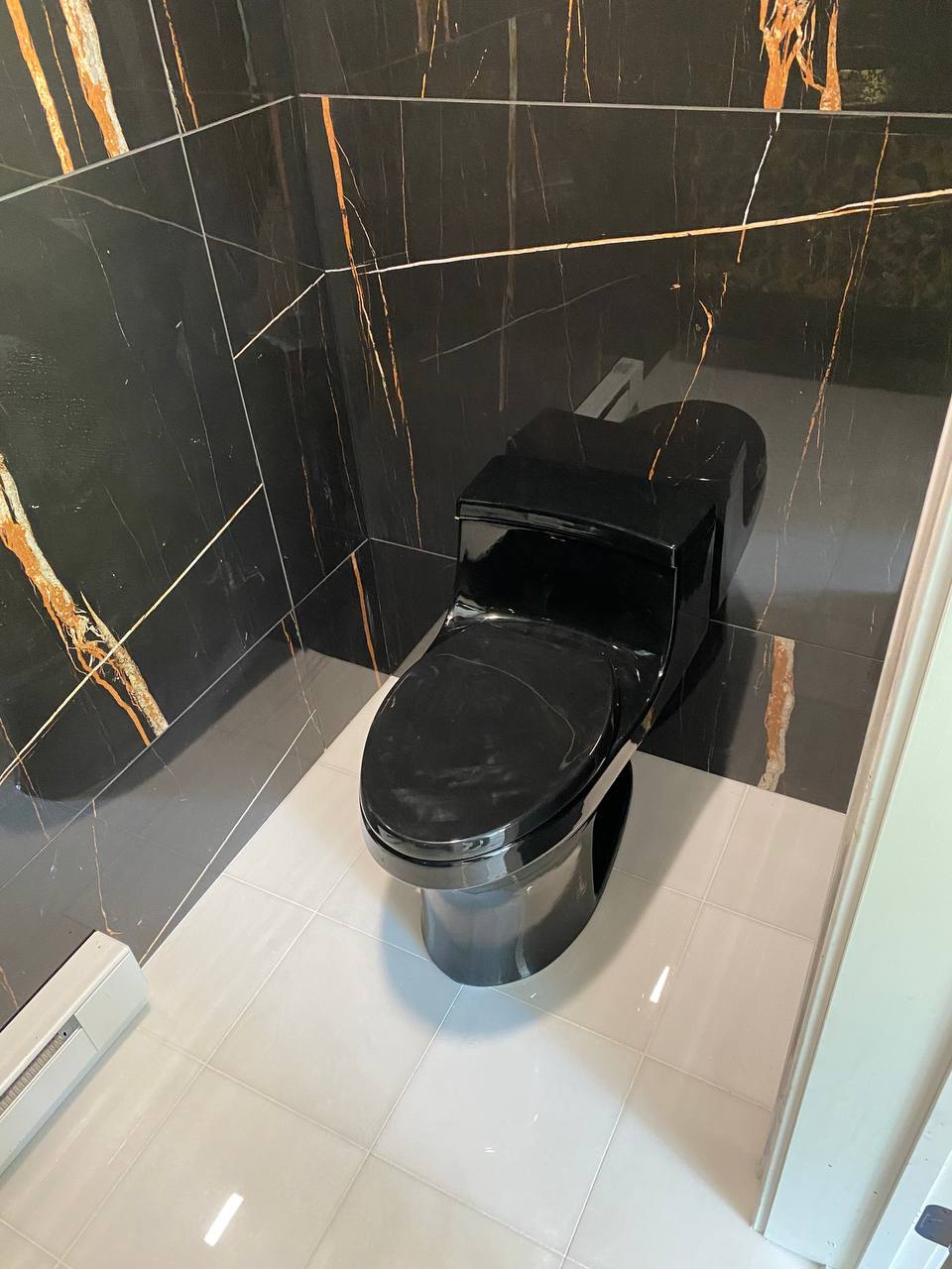 Black one-piece toilet against black and gold marble-look tile walls