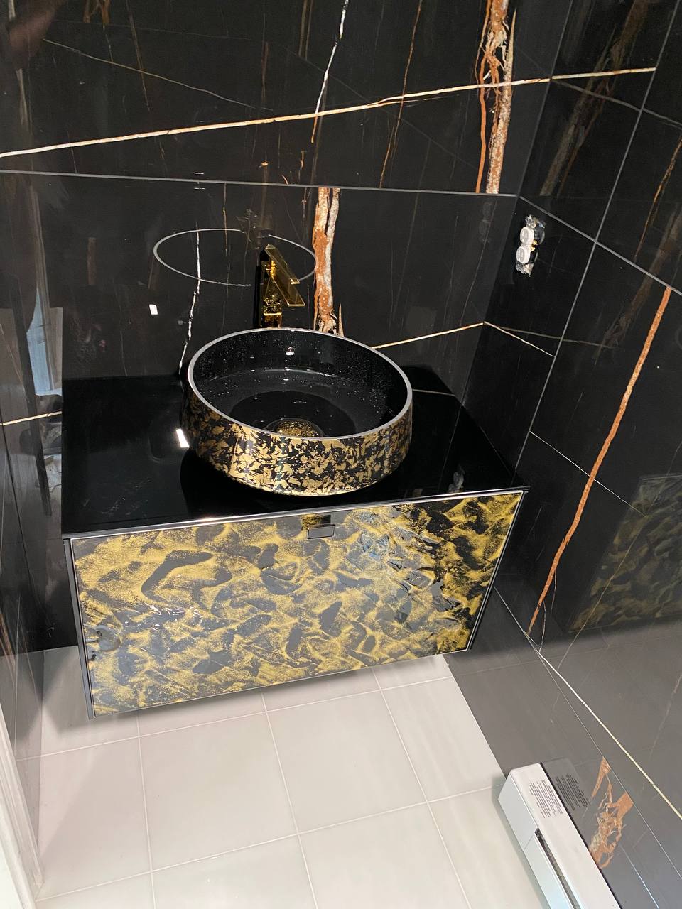 Black and gold vessel sink on floating vanity against black marble-look tile
