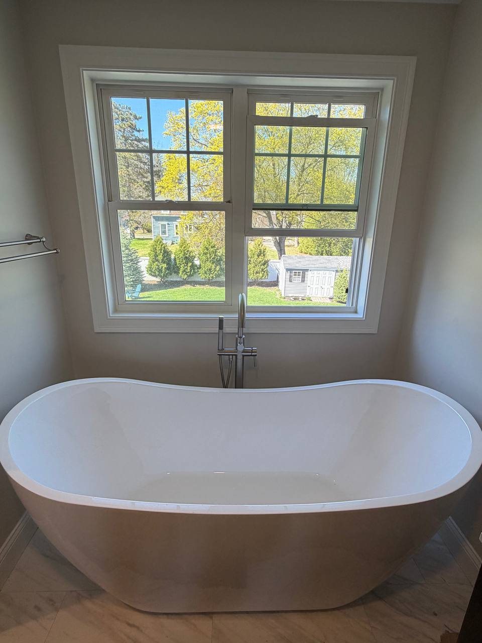 Freestanding soaking tub with floor-mounted tub filler faucet in front of a window